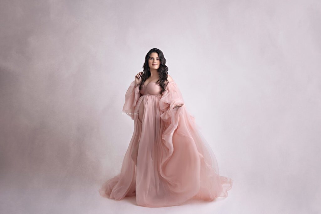 Pregnant mother in flowing blush gown with soft lighting, luxury south atlanta maternity photography studio