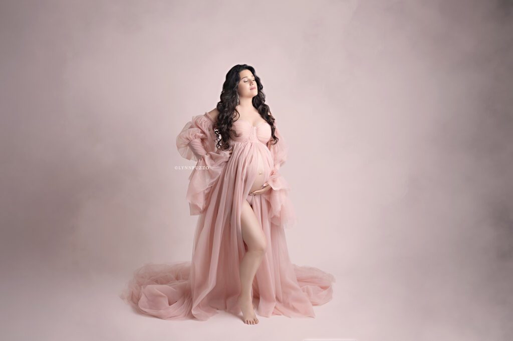Pregnant mother in flowing blush gown with soft lighting, luxury south atlanta maternity photography studio